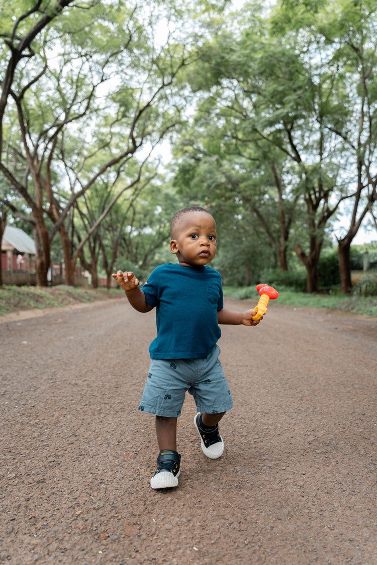 Representación actoral de un niño pequeño sosteniendo un juguete al aire libre mientras camina